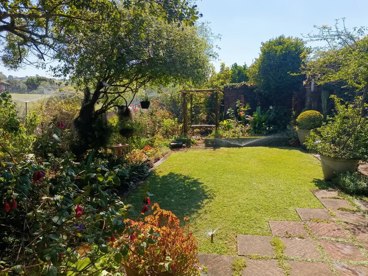 A healthy, vibrant garden in Howick maintained by an automatic sprinkler system, featuring a green lawn, established trees, and a wooden pergola.